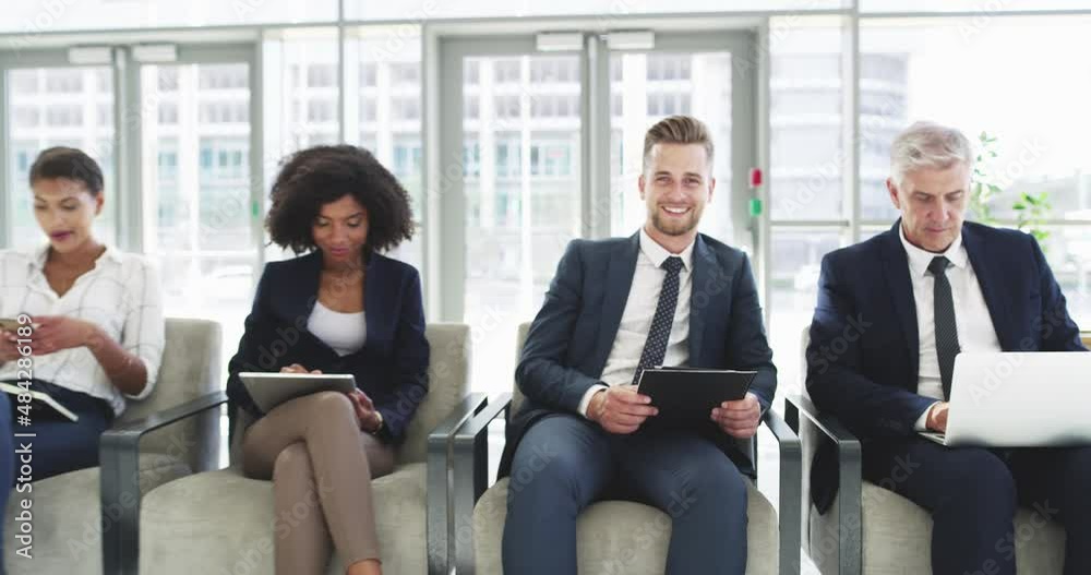 Group of businesspeople using digital devices while sitting in a line. Group of four diverse businesspeople sitting in chairs in a row using technology in an office at work. Group of businesspeople using digital devices while sitting in a line. Group of four diverse businesspeople sitting in chairs in a row using technology in an office at work.