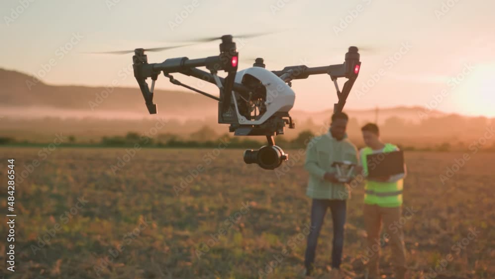 Agribusiness innovations. Flying drone in agricultural farm. Two multi-ethnic engineers control copter with tablet and laptop, checking soil and harvest. Agribusiness innovations. Flying drone in agricultural farm. Two multi-ethnic engineers control copter with tablet and laptop, checking soil and harvest.