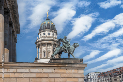 Statue of winged harpist riding a lion outside the Konzerthaus in Berlin, cathedral dome in background,  daytime, sunny, nobody photo