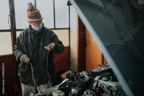 Old man with protective mask in the garage repair his old car.