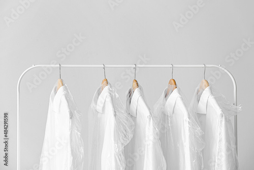 Rack with clean shirts in plastic bags on grey background © Pixel-Shot