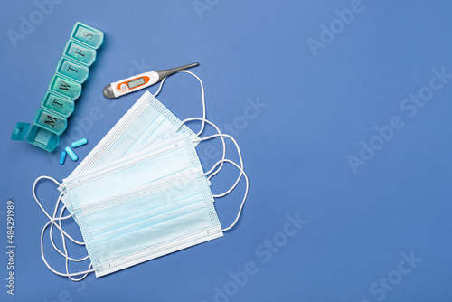 Medical masks, thermometer and capsules on color background