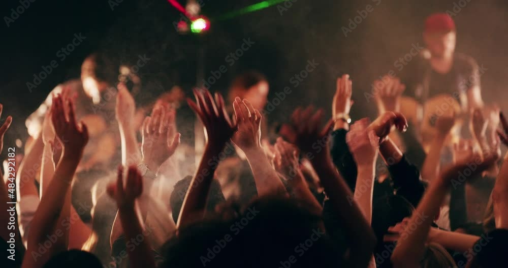 The band that brought everyone together. Group of young, fun loving people celebrating and dancing under strobe lights. Crowd cheering with hands raised at a festival, concert, party, or rave