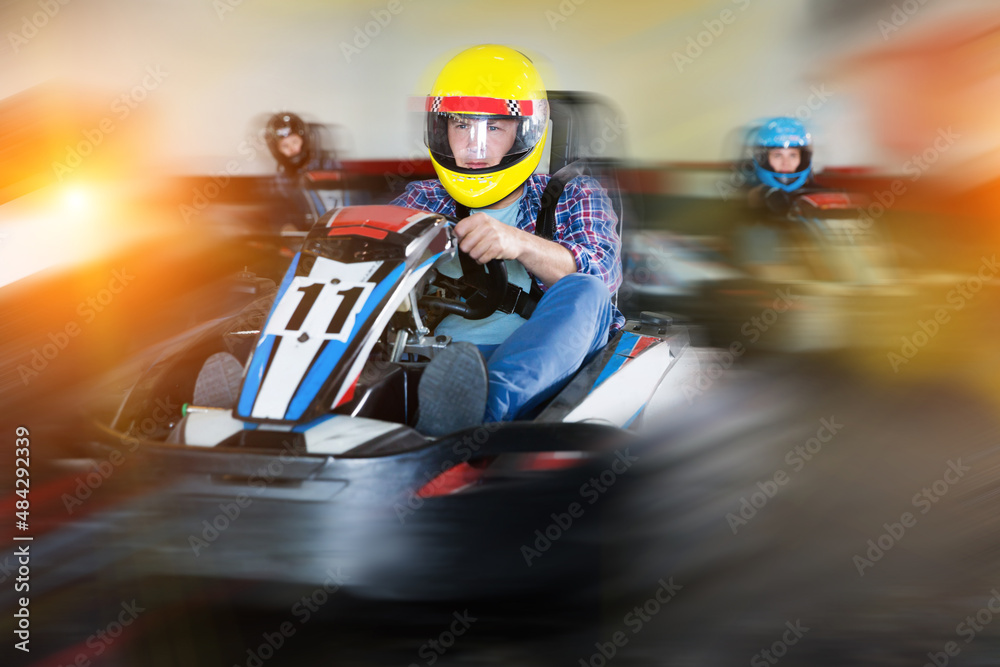 adult man in helmet and other people driving car for karting in sport club indoor