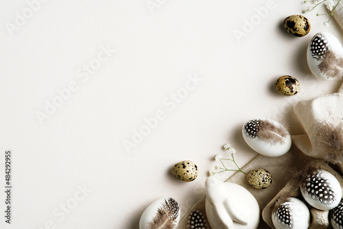 Minimal Easter concept. Easter eggs decorated feathers with cloth, bunny rabbit and gypsophila flowers on white background. Stylish Easter card design.
