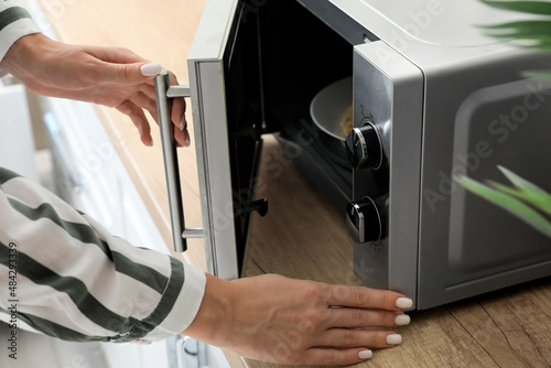 Young woman opening modern microwave oven in kitchen