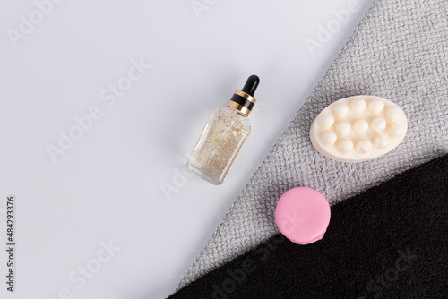 Handmade white massage soap and pink macaroon soap on gray and black terry towels. Bath accessories. Face serum with gold