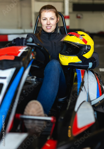 Smiling woman with helmet sitting in go-kart car in karting club