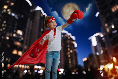 Little girl wearing superhero costume and beautiful cityscape in night on background