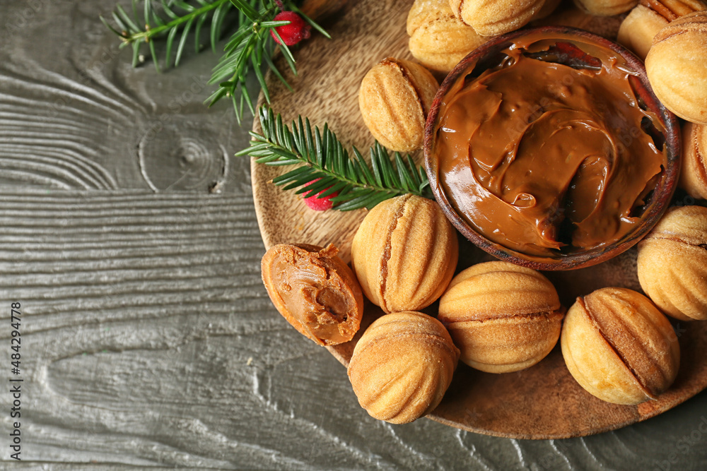 Plate of tasty walnut shaped cookies with boiled condensed milk and fir branches on dark wooden background, closeup Plate of tasty walnut shaped cookies with boiled condensed milk and fir branches on dark wooden background, closeup