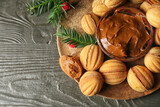 Plate of tasty walnut shaped cookies with boiled condensed milk and fir branches on dark wooden background, closeup