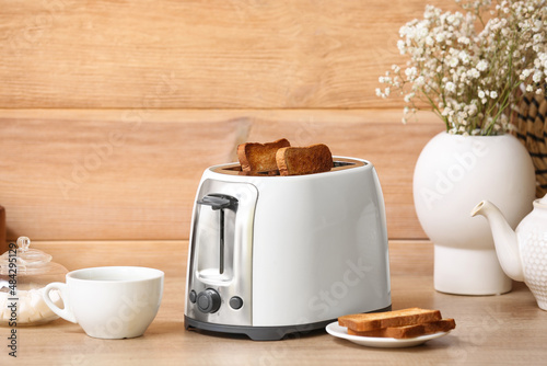 White toaster with bread slices, cup of coffee and vase on table near wooden wall