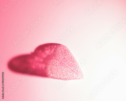 Pink leaf with heart shaped shadow on gradient pink color background. Romantic Valentines day composition. Flat lay. Love concept.