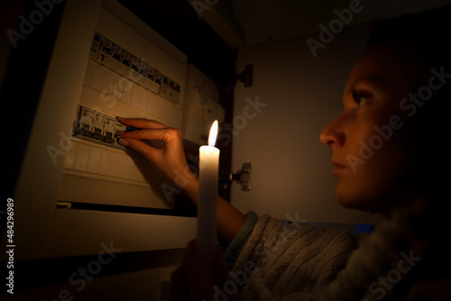 Woman in total darkness investigating fuse box at home during power outage or blackout. No electricity concept photo