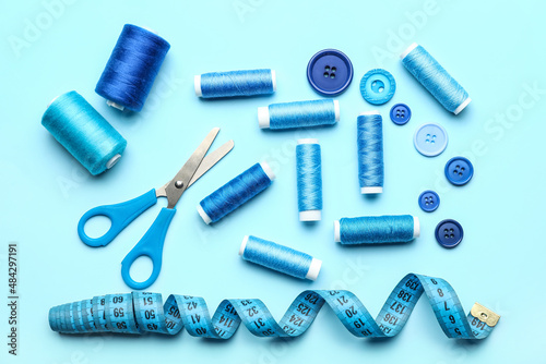 Sewing thread spools, buttons, scissors and measuring tape on color background