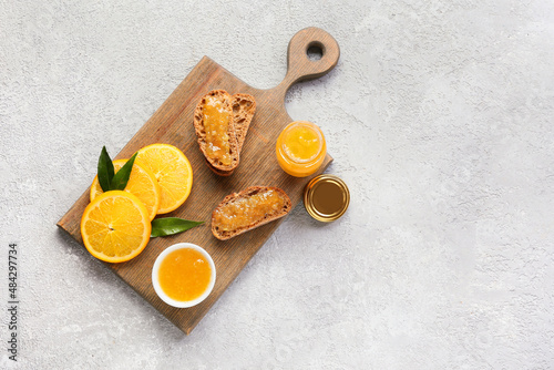 Tasty orange jam and bread on light background