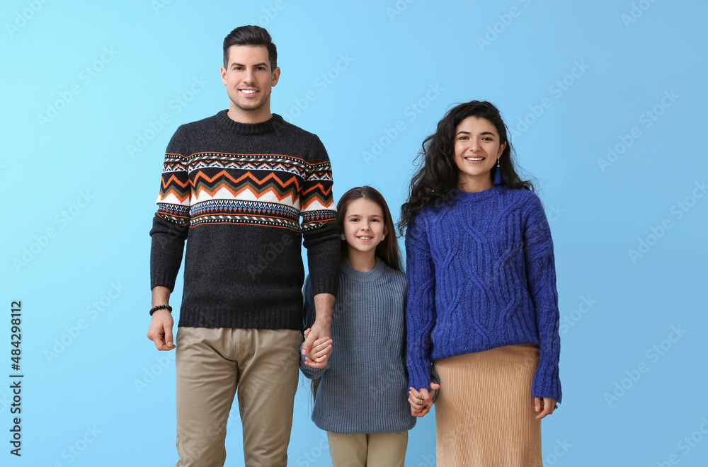 Little girl and her parents in warm sweaters holding hands on blue background