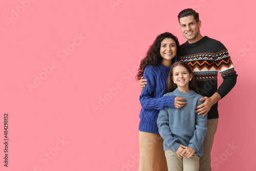 Little girl with her parents in warm sweaters hugging on pink background