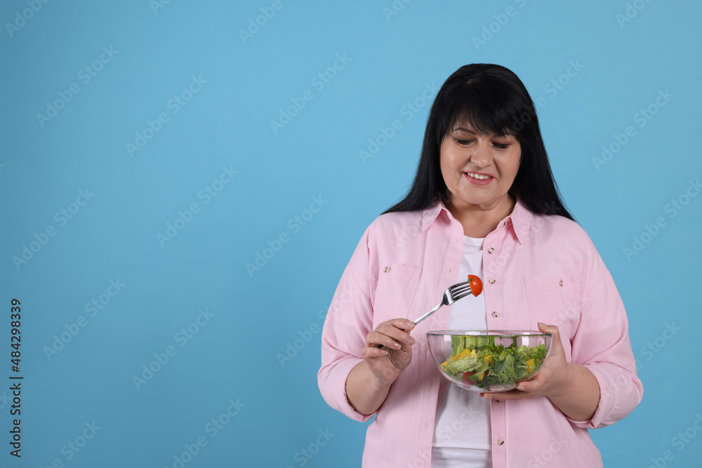 Beautiful overweight woman eating salad on light blue background, space for text. Healthy diet Beautiful overweight woman eating salad on light blue background, space for text. Healthy diet