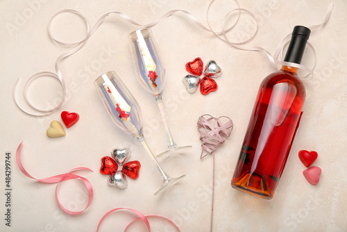 Wine bottle, glasses and chocolate candies in shape of heart on light background. Valentine's Day celebration