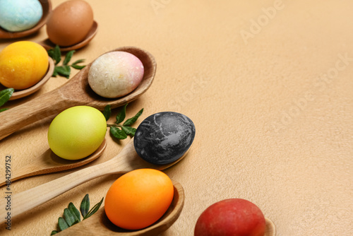 Spoons with painted Easter eggs on color background
