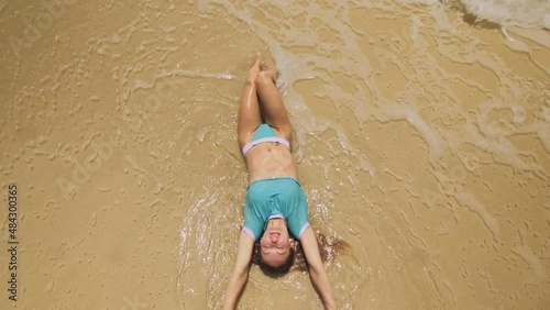 Woman lying on shallow water sea. Happy slightly tipsy woman enjoying her vacation on a tropical island. Girl funny posing. Top view