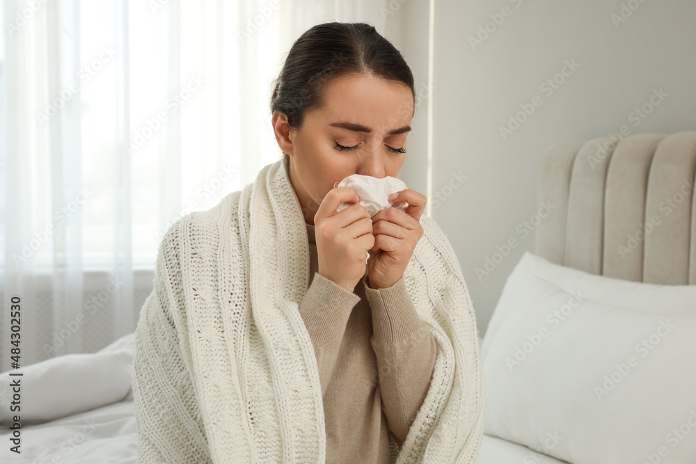 Sick young woman with tissue wrapped in knitted plaid at home Sick young woman with tissue wrapped in knitted plaid at home