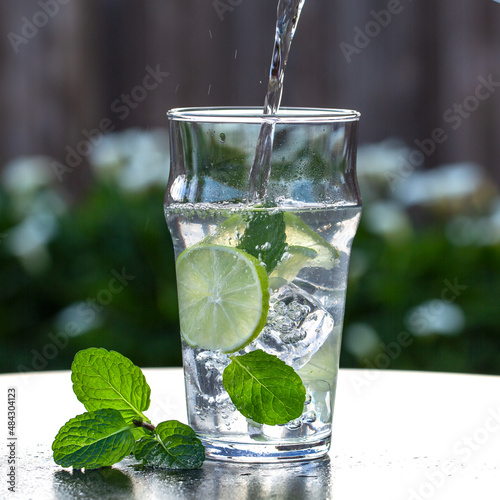 Pouring Fresh Water with Lime and Mint on Ice Out in the Garden
