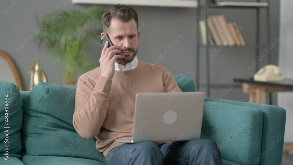 Man with Laptop Talking on Smartphone on Sofa 