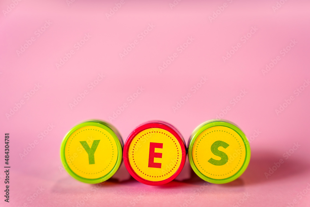 Fototapeta premium Word YES in letters text from kid's toy stamps isolated on a pink background
