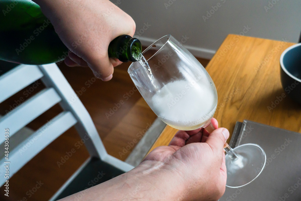 Pouring champagne in glass at home dinner table.
