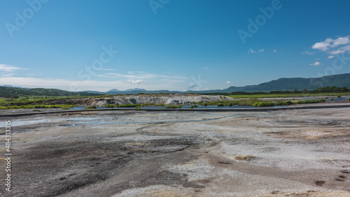 Hot streams flow in the caldera of an extinct volcano. There are sulphurous deposits on the soil. There is a wooden path for tourists. A mountain range against a blue sky. Kamchatka. Uzon