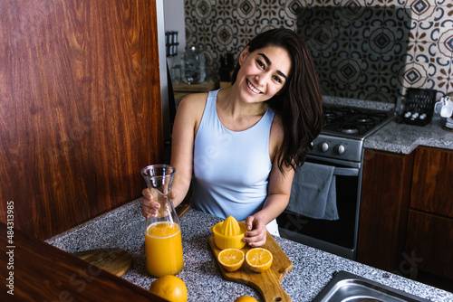 Schilderij op canvas Hispanic brunette young latin woman preparing orange juice at the kitchen in Mex