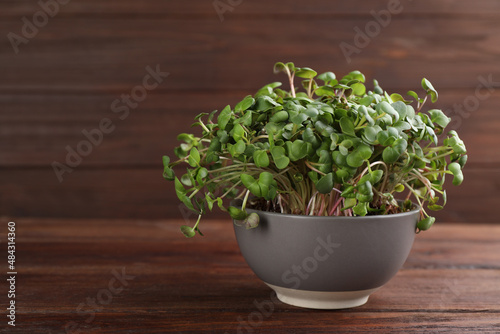 Fresh radish microgreens in bowl on wooden table, space for text