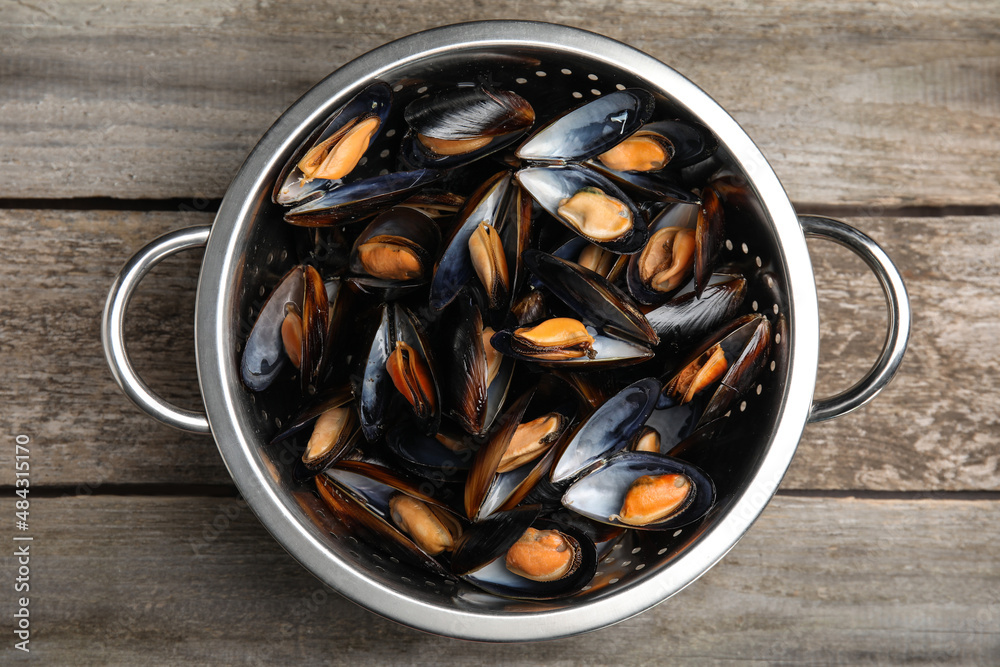 Colander with delicious cooked mussels on wooden table, top view