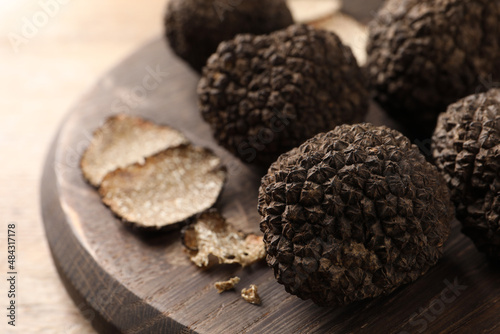 Whole and cut black truffles with wooden board on table, closeup