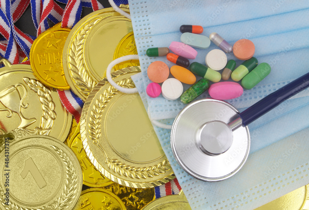 Face masks with stethoscope and drugs on gold medals background. Sport competitions in coronavirus pandemic time. Face masks with stethoscope and drugs on gold medals background. Sport competitions in coronavirus pandemic time.