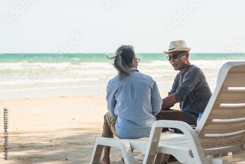 Happy Asian family, senior couple sitting on chairs with backs on beach travel vacation talking together, Romantic elderly enjoy Travel summer vacation, plan life insurance retirement couple concept © sorapop