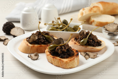 Delicious bruschettas with truffle sauce and caperberries on white wooden table, closeup