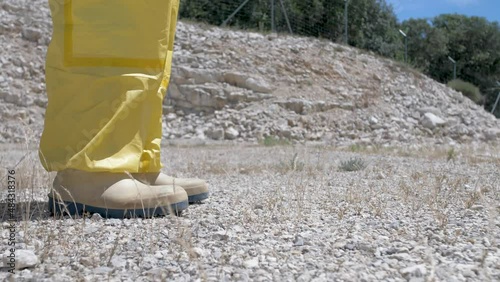 Man legs with hazmat suit walking on arid terrain with weeds, Dolly right ground shot photo