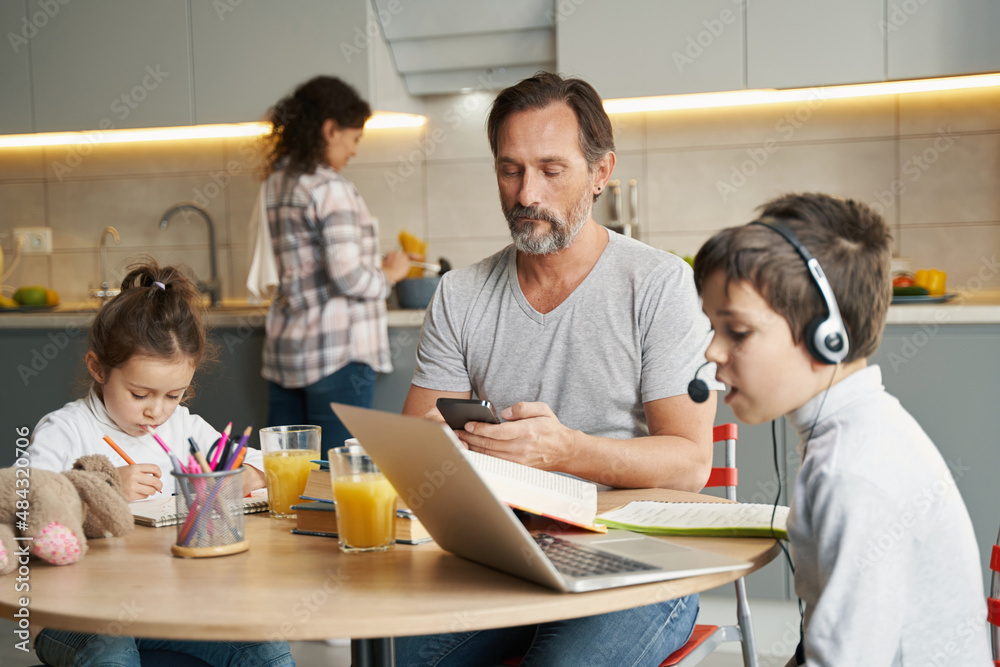 Father using smartphone while his kids doing homework Father using smartphone while his kids doing homework