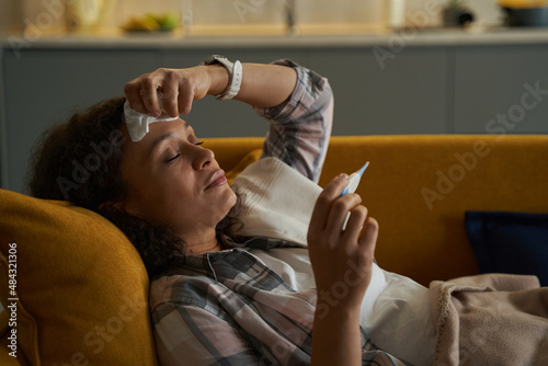 Female having an illness checking her temperature with thermometer photo