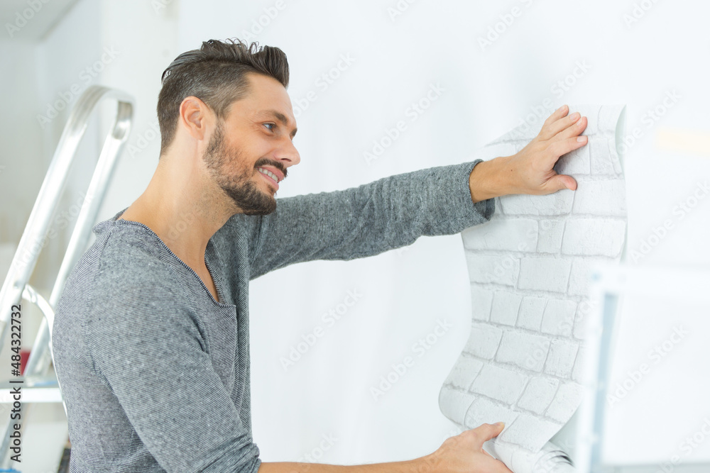 handyman putting up wallpaper on the white walls