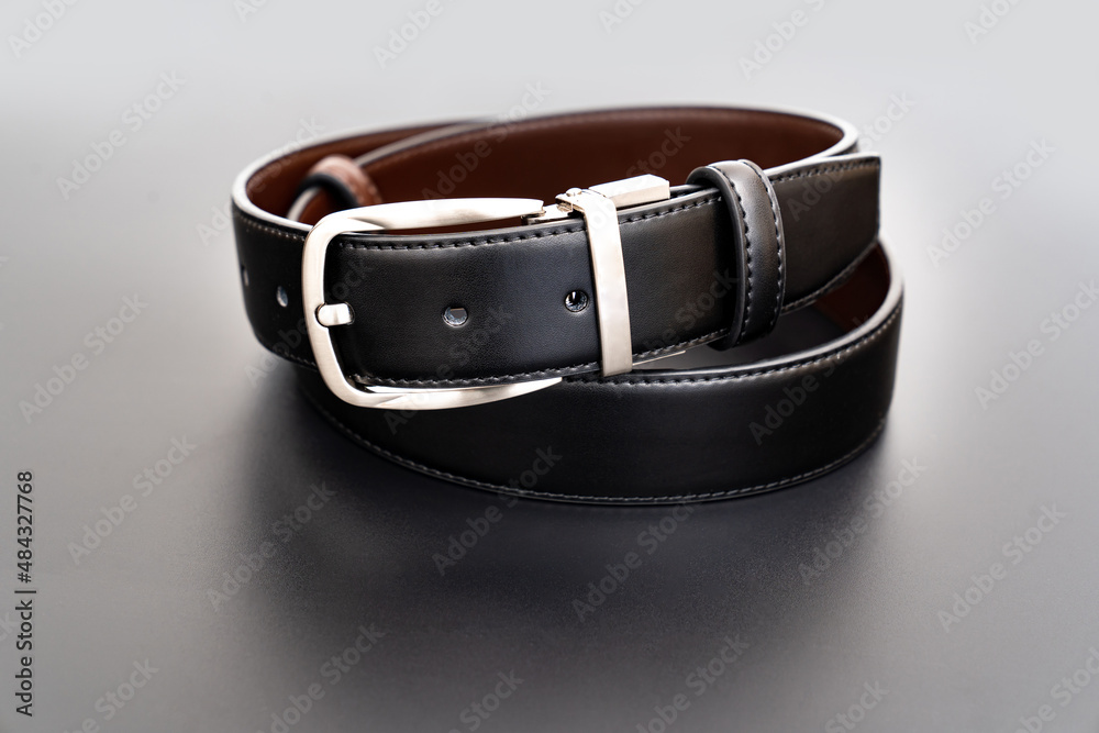 Double-sided black and brown leather belt with an unbuttoned buckle on a black background. Double-sided black and brown leather belt with an unbuttoned buckle on a black background.