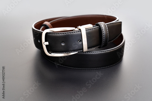 Double-sided black and brown leather belt with an unbuttoned buckle on a black background.