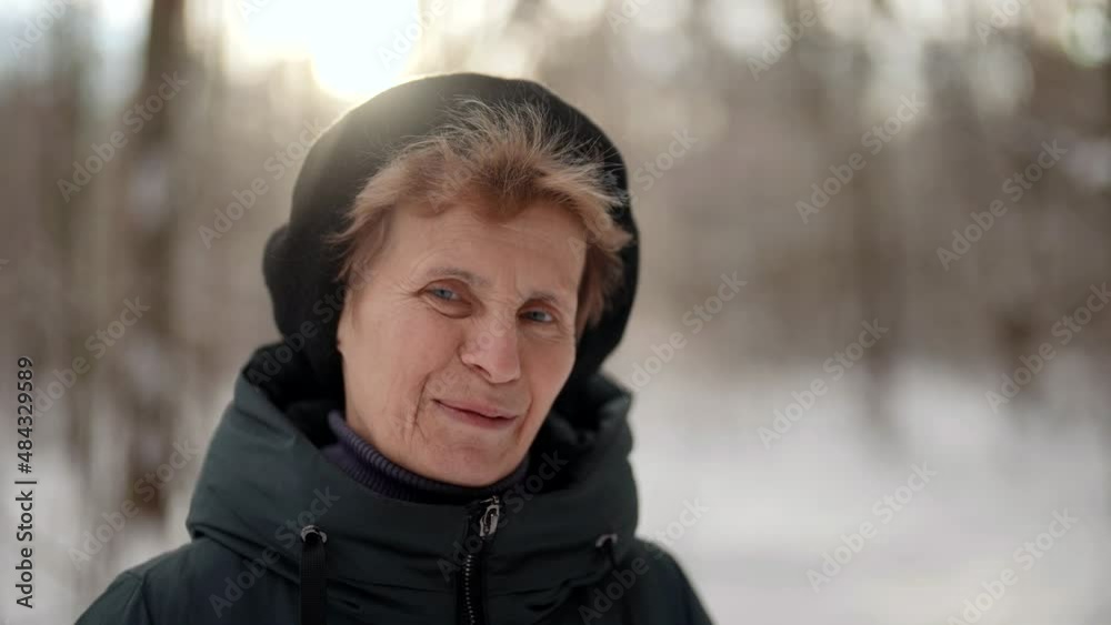 smiling old woman is standing alone on street in park in winter day, looking at camera calmly smiling old woman is standing alone on street in park in winter day, looking at camera calmly