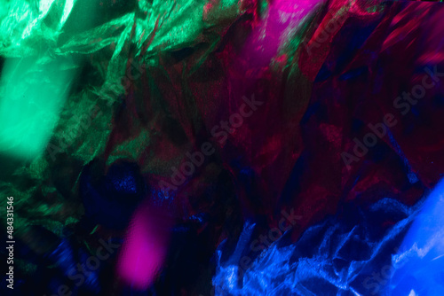 Blur color background. Creased texture. Distressed material. Defocused neon light magenta pink green blue glow defect on dark shiny rough foil structure grunge overlay.