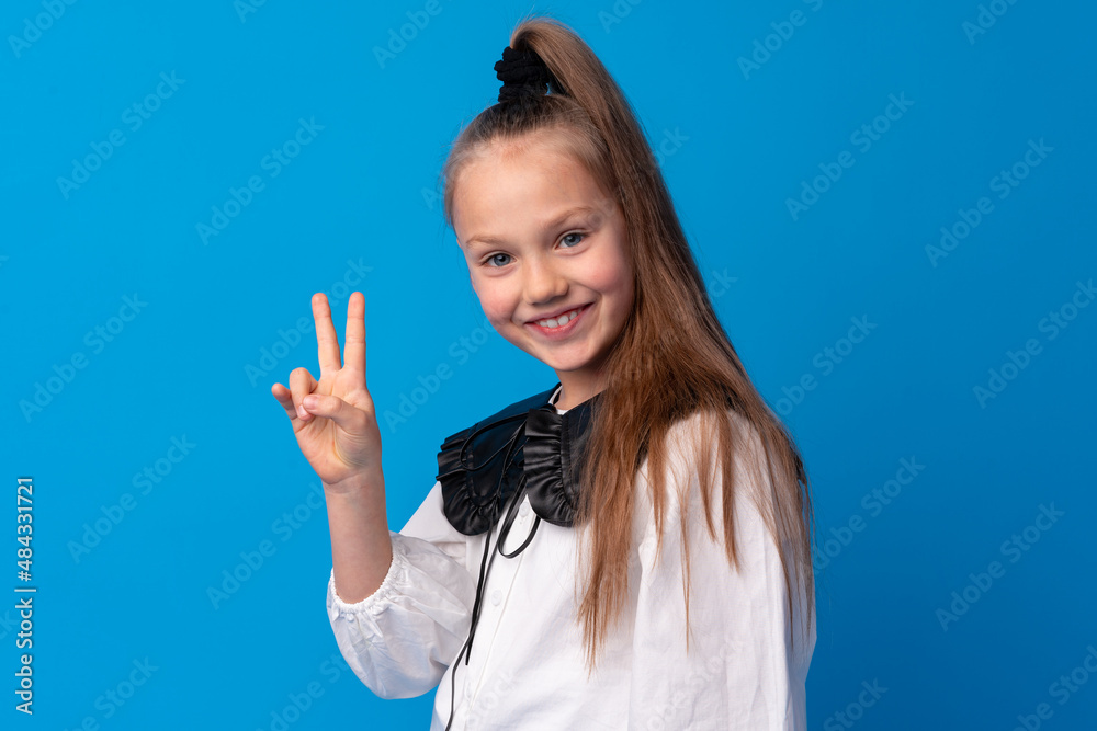 Young teen girl showing a peace symbol with fingers against blue background