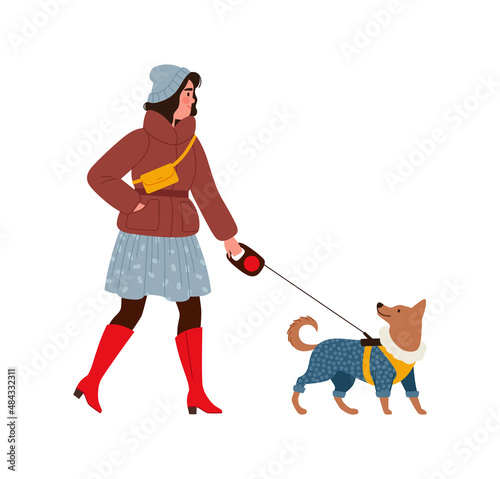 Young woman in fashionable winter clothes walks a dog in a jacket on a leash. A girl in red high boots, a skirt and a jacket on a walk with a pet in the winter season