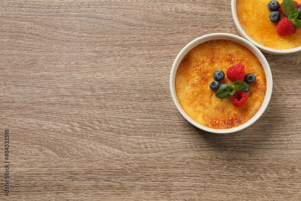 Delicious creme brulee with fresh berries on wooden table, flat lay. Space for text Delicious creme brulee with fresh berries on wooden table, flat lay. Space for text